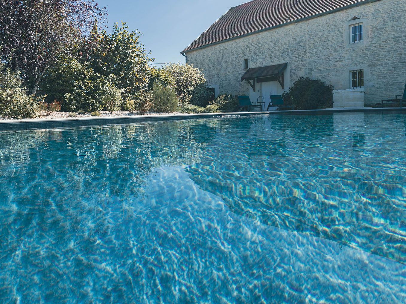 piscine ensoleillée avec maison ancienne et végétation